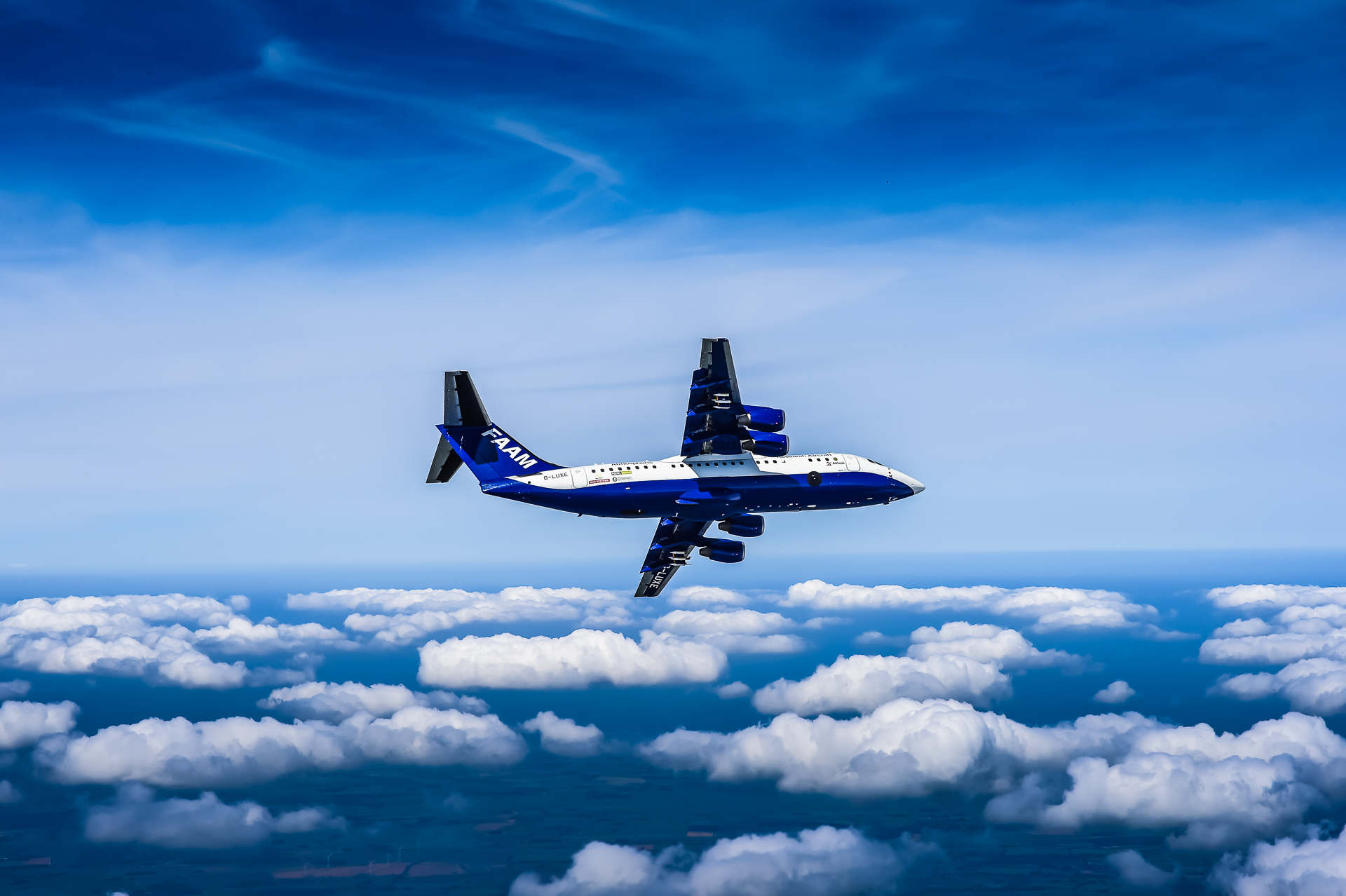 A blue and white research aircraft banking away from the camera, above small white clouds