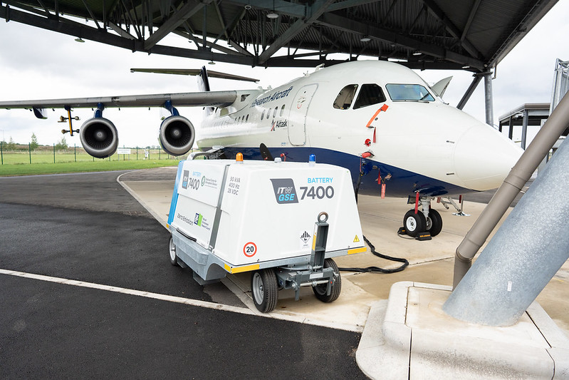 Electric ground power unit in front of a blue and white research aircraft. There is a black power cable connecting the power unit to the aircraft.