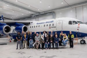 A group of people sit and stand in front of an aircraft in a hangar.